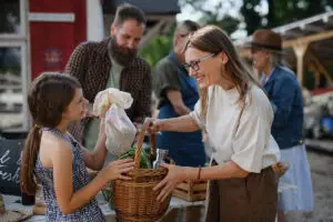 Little girl with her mother buying organic vegetables in a tight-knit community.