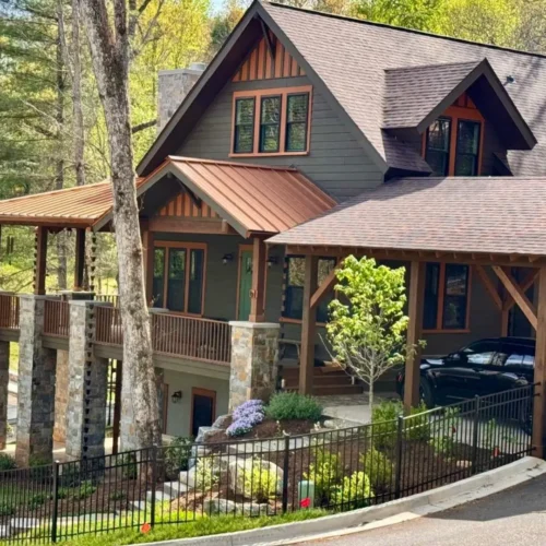 Craftsman-style home with elevated covered porch, stone pillars, wood accents, and carport, set on a landscaped corner