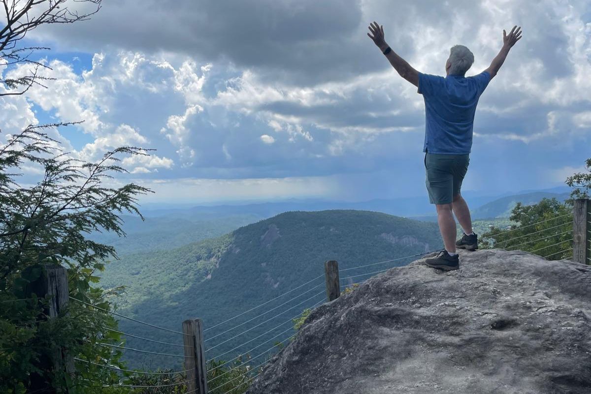 Man on mountain overlook with arms raised